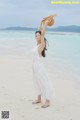 A woman in a white dress and straw hat on the beach.